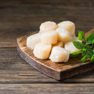 raw fresh domestic U10 scallops on a wooden cutting board on a wooden table